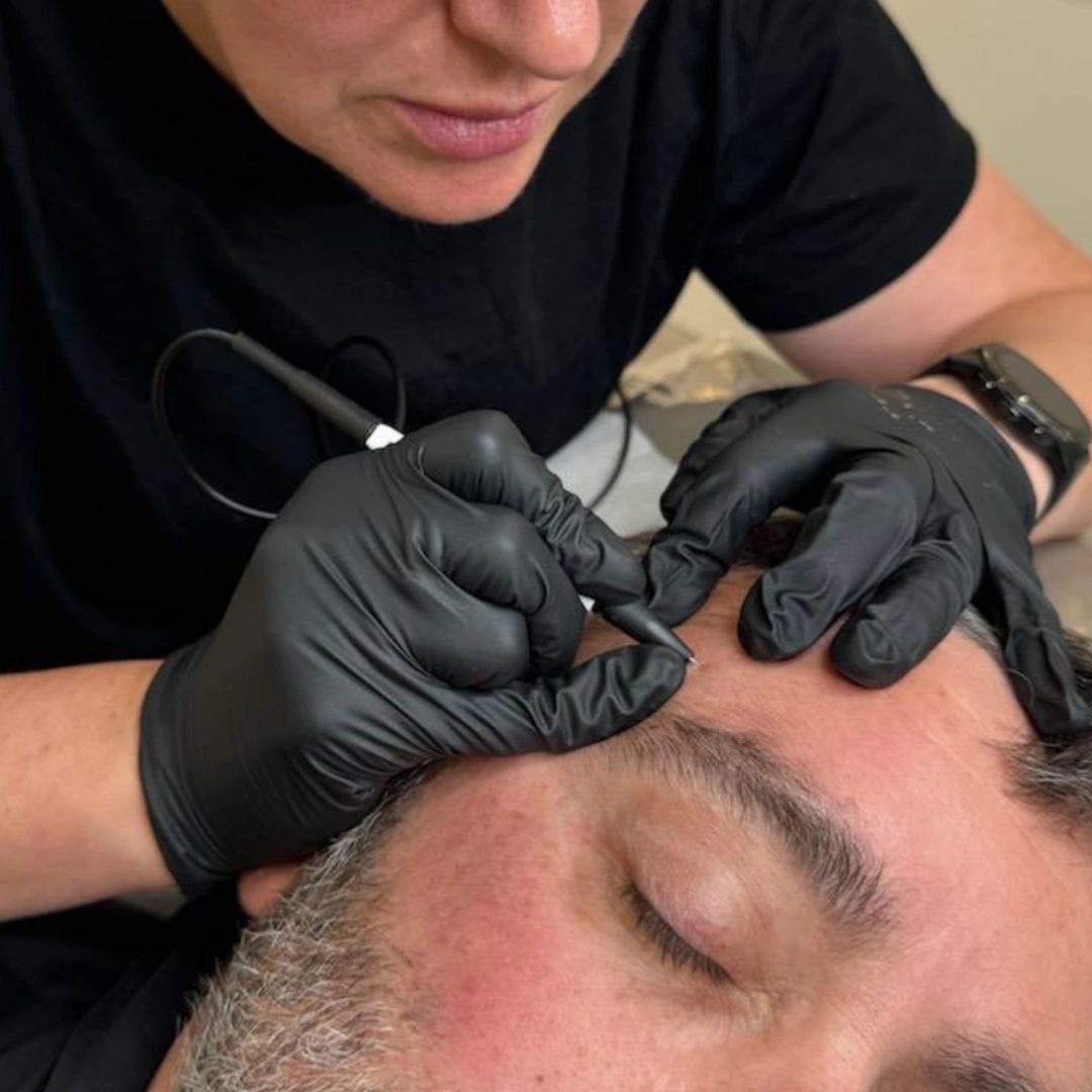 Close-up of cosmetic tattoo procedure on man's eyebrow.