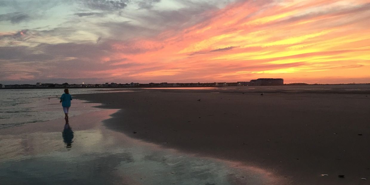 Person walking alone on a beach at sunset.