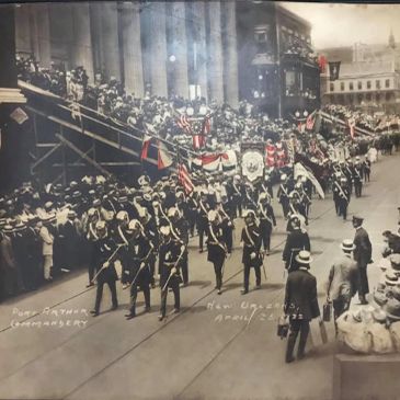 Historic parade with marching soldiers and spectators in early 20th-century attire.