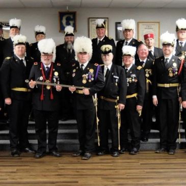 Group of men in formal uniforms with feathered hats posing indoors.