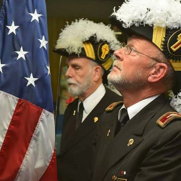 Two veterans in uniform stand solemnly by the American flag.