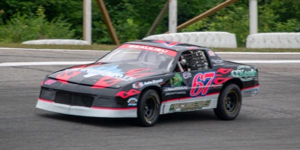 Black and red race car with number 67 on a track.