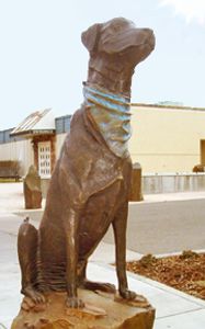 Bronze statue of a Labrador sitting on a rock with a bandana around his neck