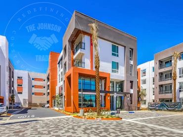 Modern apartment complex with vibrant orange accents and palm trees under a clear blue sky.