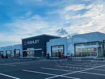 Empty parking lot in front of a modern Ashley furniture store under a blue sky.