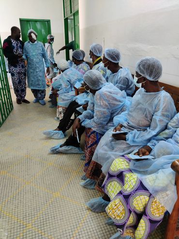 Patients in protective gowns and hairnets waiting in a hospital corridor.