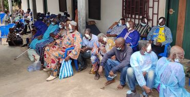 Group of people with eye patches waiting outdoors on chairs and the ground.