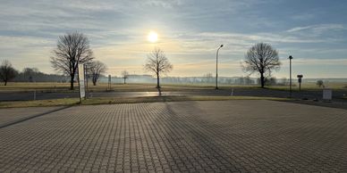 Sun shining over a paved area with leafless trees and open fields.