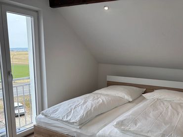 Minimalist bedroom with twin beds and large window overlooking green fields.