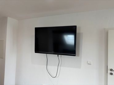A wall-mounted flat screen TV with two hanging cables in a minimalistic room.