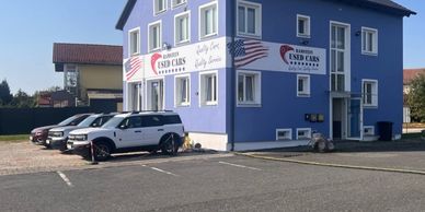Blue building with signs for a used car dealership and several parked cars outside.