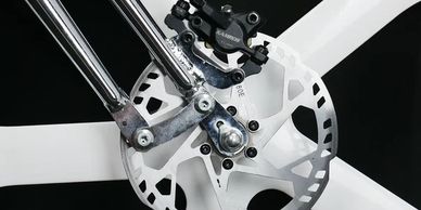Close-up of a bicycle disc brake on a white wheel with chrome parts.