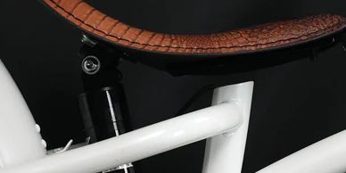 Close-up of a white bike frame with a brown textured leather saddle.