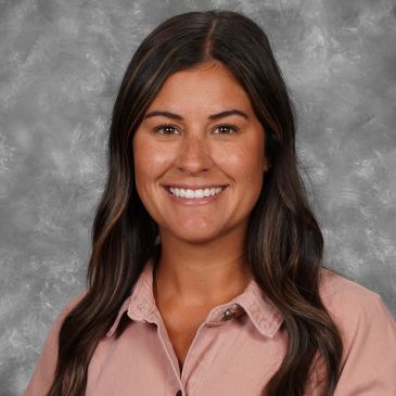 Smiling woman with long dark hair wearing a light pink shirt.
