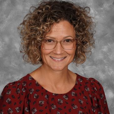 Smiling woman with curly hair and glasses.