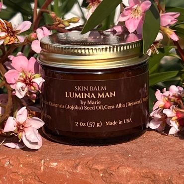 Jar of Lumina Man skin balm surrounded by pink flowers outdoors.