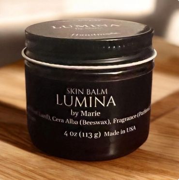 A jar of Lumina skin balm by Marie on a wooden surface.