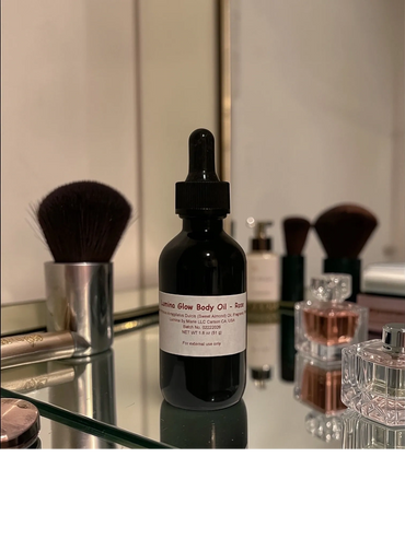 A bottle of Lumina Glow Body Oil with makeup brushes and perfume on a mirrored surface.