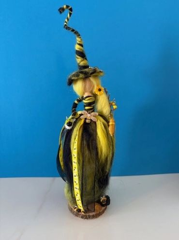 Decorative witch doll with yellow and black attire against a blue background.