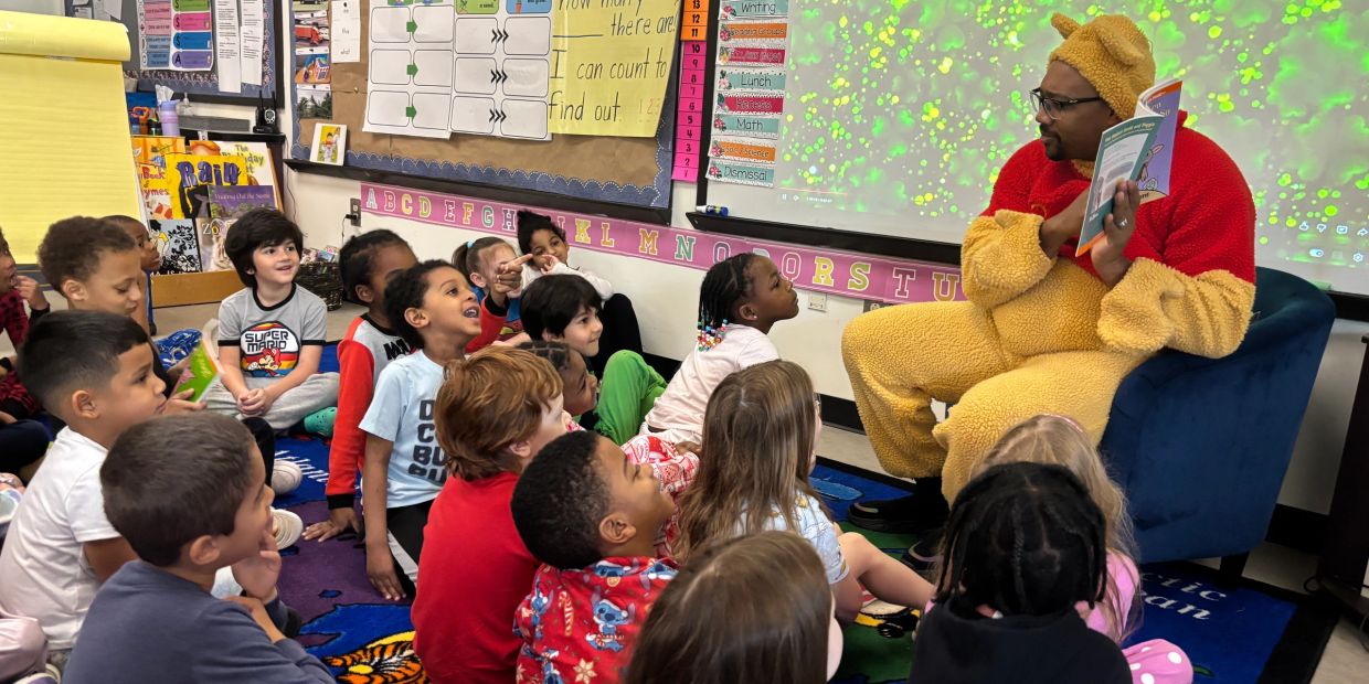 Man in Winnie the Pooh costume reading to children in classroom.