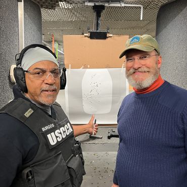 Two men at a shooting range showing a target with bullet holes.