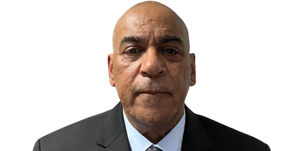 Serious man in a black suit and patterned tie against a black background.