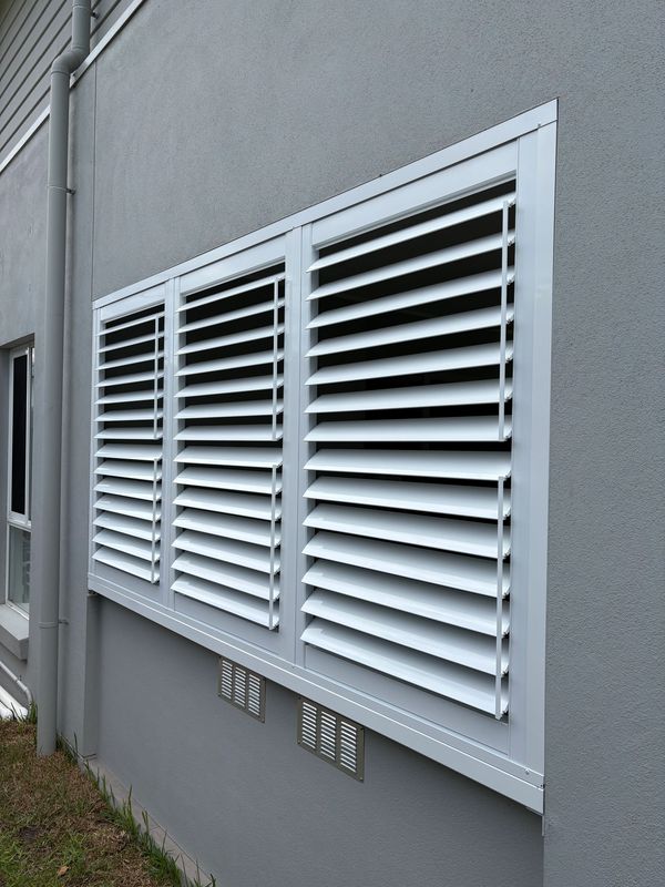 White louvered window shutters on a gray exterior wall.
