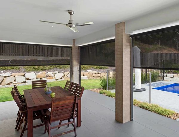 Covered outdoor dining area with wooden table and chairs beside a pool.