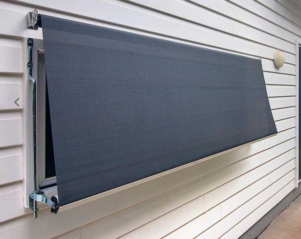 Retractable dark gray window awning on a white siding exterior wall.