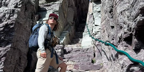 Luca stands at the base of the steps to Comeau Pass in hiking gear.
