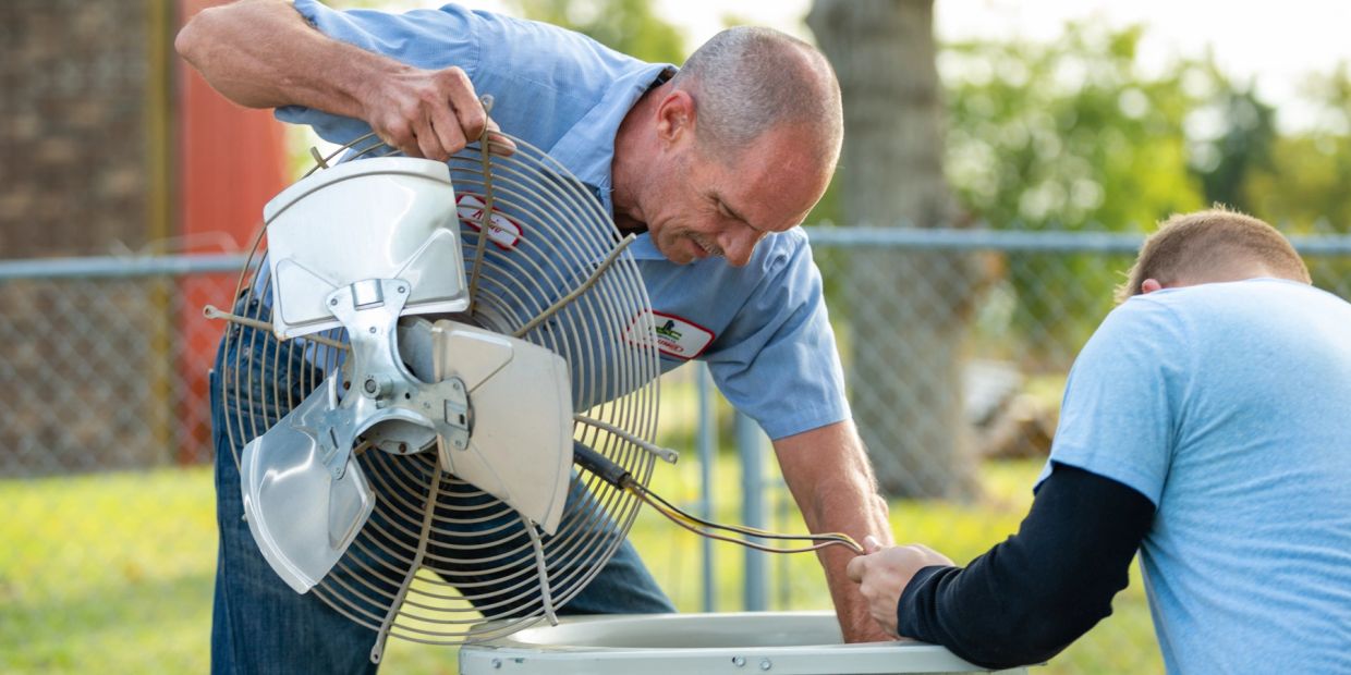 Two men repairing an air conditioning unit outdoors.