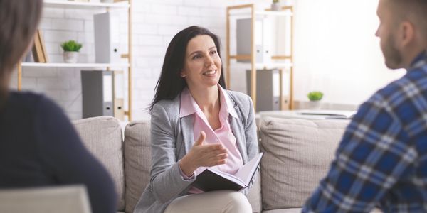Woman counselor speaking to a couple on a couch in a bright office.