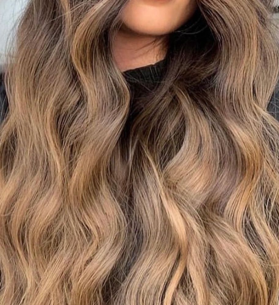 Woman with long, wavy, highlighted hair posing indoors.