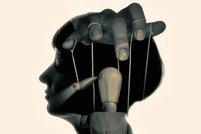 Silhouette of human head with a hand as the brain pulling puppet strings