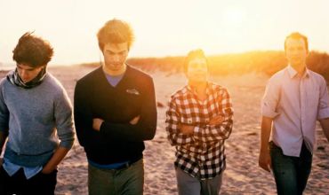 Four young men walking on the beach at sunset.