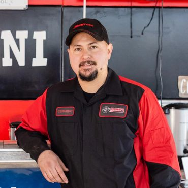 Mechanic named Gerardo in a red and black uniform, smiling in a workshop.