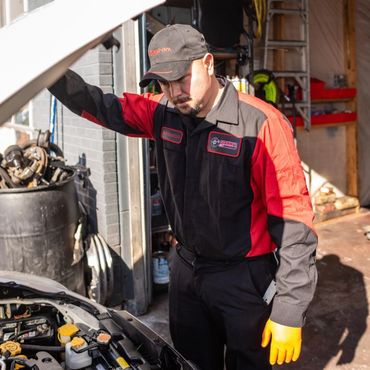 Mechanic in black and red uniform inspecting a car engine.