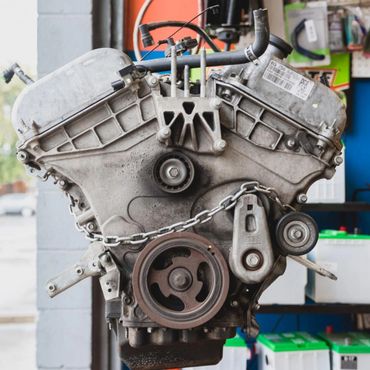 A used car engine hanging in a workshop with tools and batteries in the background.