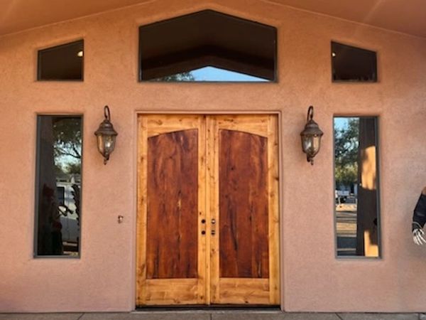 Rustic double wooden doors with side windows on a stucco house exterior.