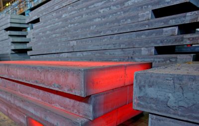 Stacked steel slabs with a glowing red-hot one in an industrial setting.