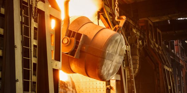 Molten metal pouring from a large industrial ladle in a foundry.