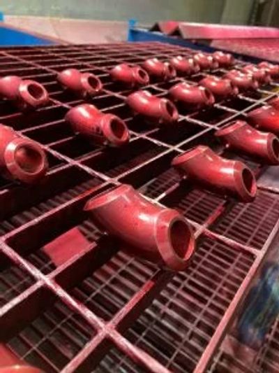 Rows of red metal pipe fittings drying on a rack.