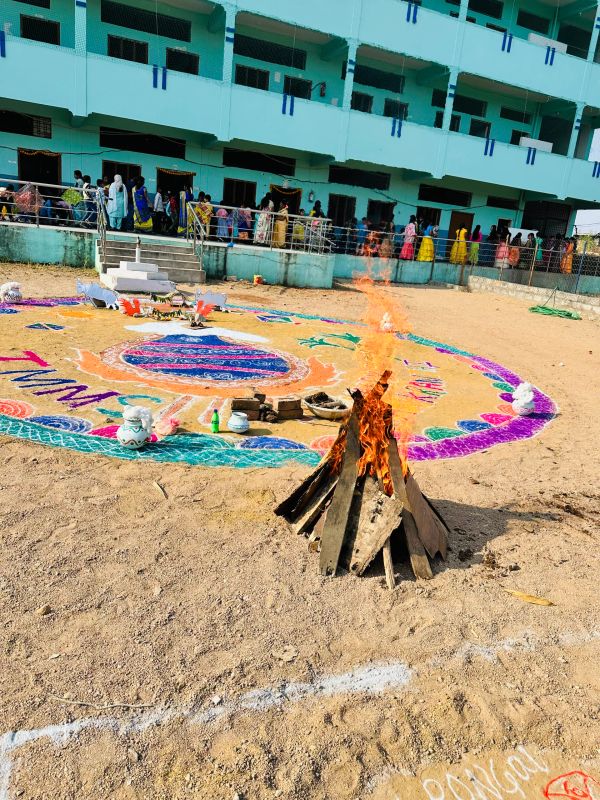 Outdoor colorful rangoli with a burning bonfire on sandy ground.