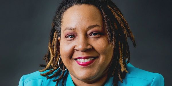 Smiling woman in turquoise blazer with hoop earrings.