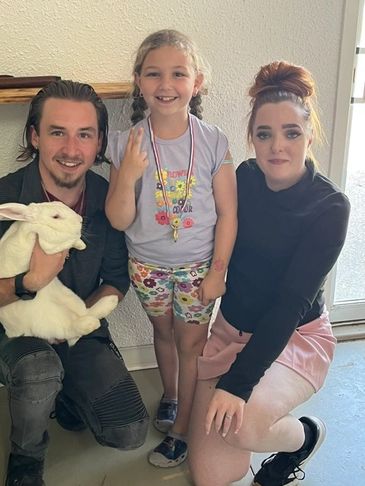 A family poses happily with a large white rabbit indoors.