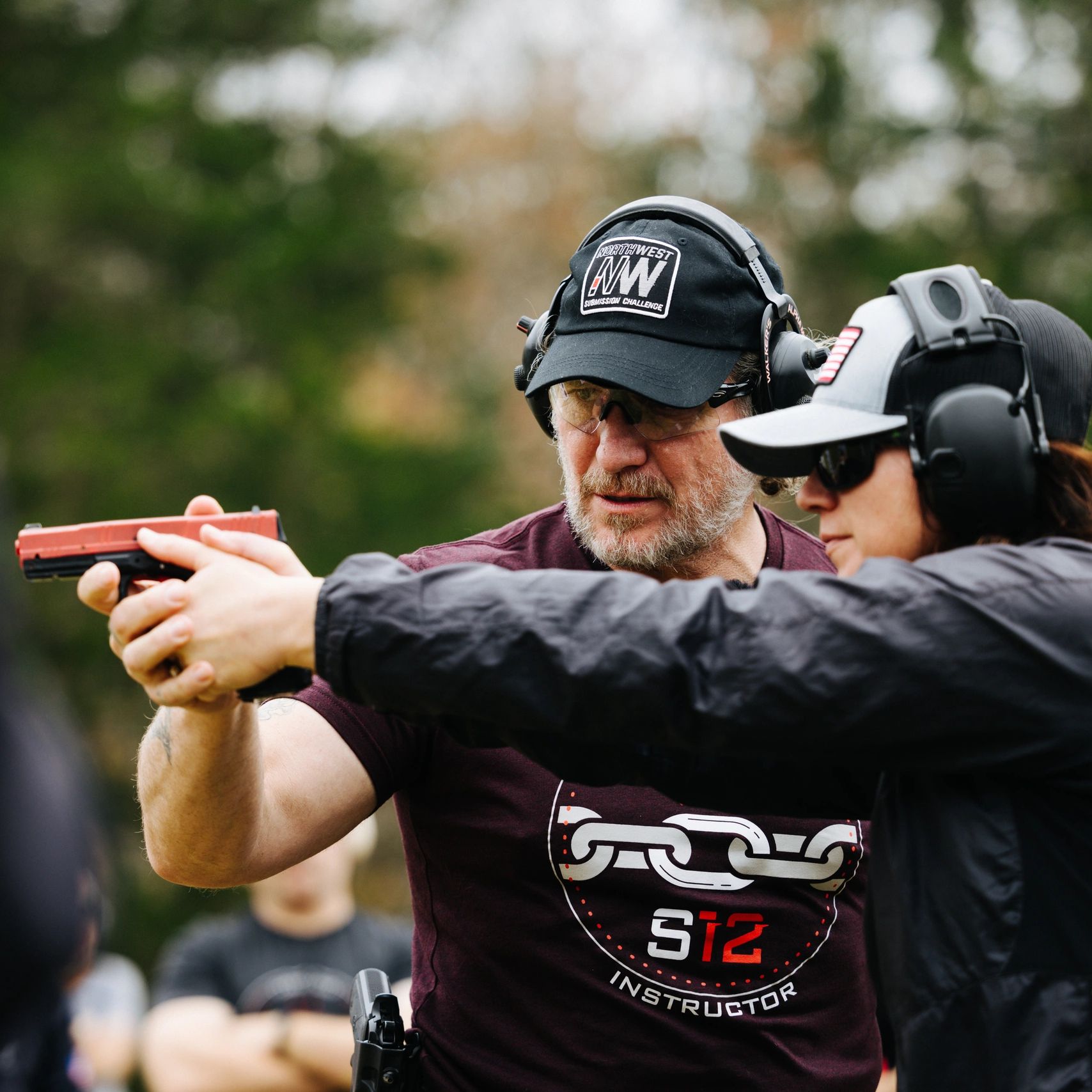 Instructor guiding a woman on firearm handling at a shooting range.