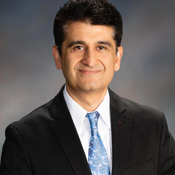 Professional man in suit and blue patterned tie smiling.