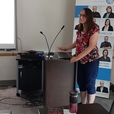 A woman standing at a podium in front of a sign looking out at the crowd (not visible).