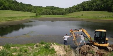 Excavator working near a pond with two men observing.