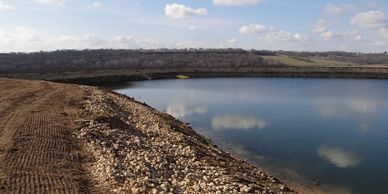 A calm lake bordered by rocky shore under partly cloudy sky.